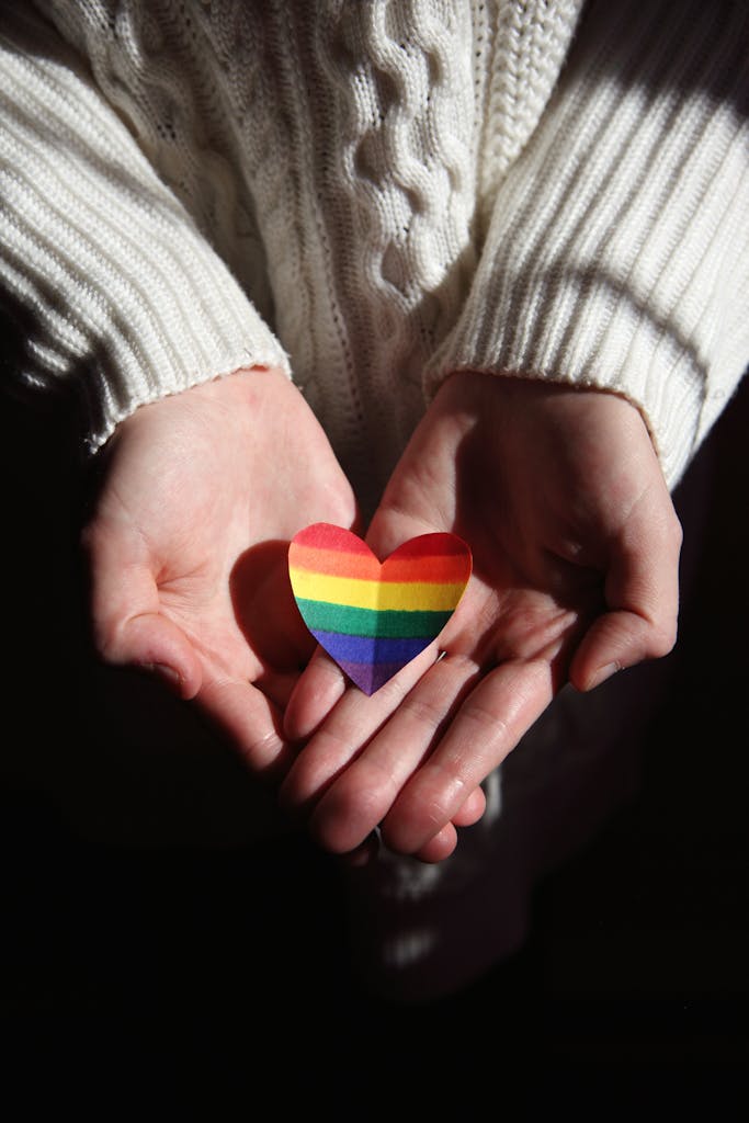 Close-up of hands cradling a rainbow heart, symbolizing love and LGBTQ+ pride.
