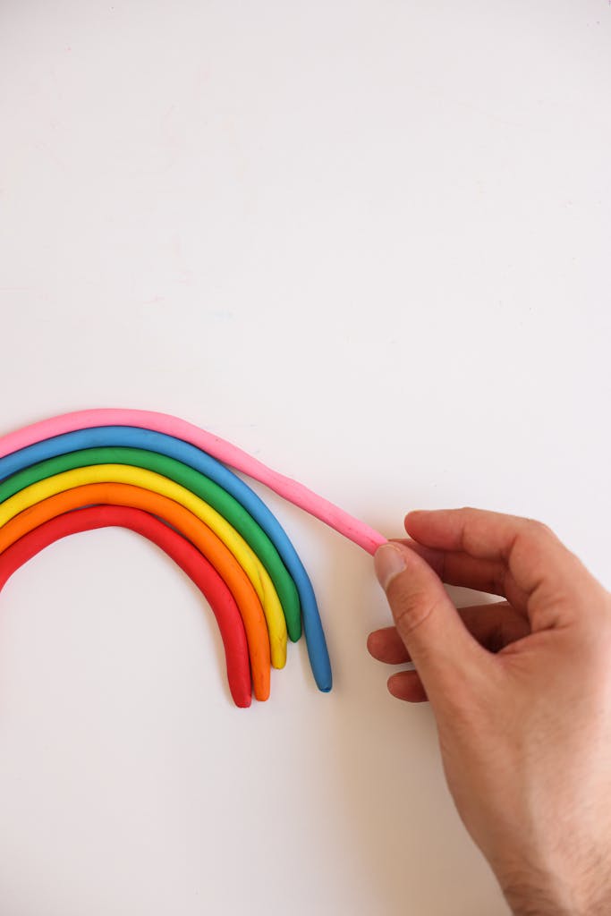 Hand arranging colorful clay rainbow on a white background.